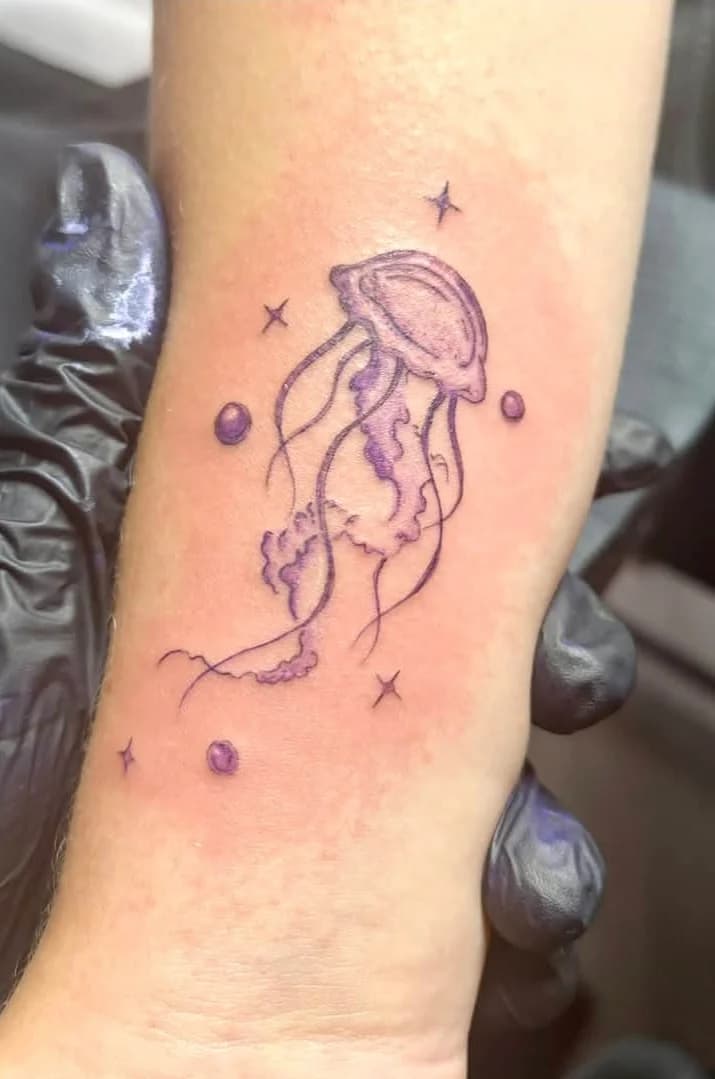 Fineline jellyfish tattoo in violet ink on a forearm